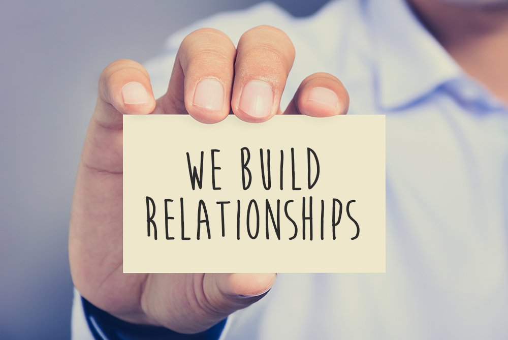 A person holding a card that says "We Build Relationships"